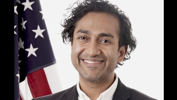 Smiling man in suit with American flag backdrop