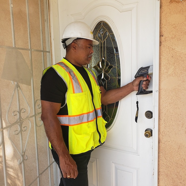 Man in hard-hat checking for lead levels in pain on a white door.