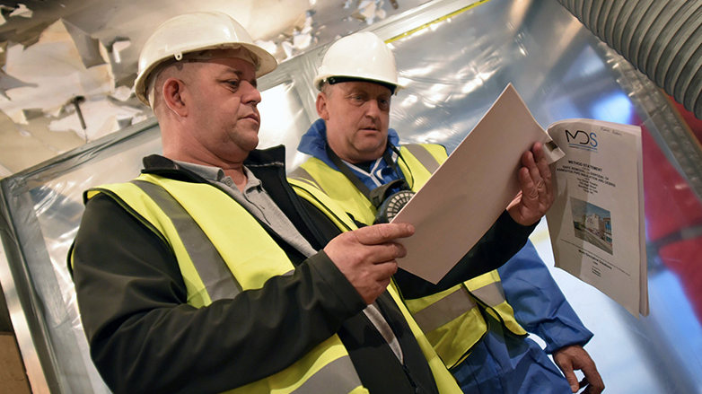 2 men in hard-hats and yellow safety vest looking at documents