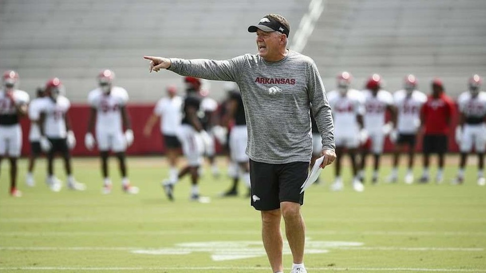 Arkansas Razorbacks coach on a football field with a vibrant stadium background.