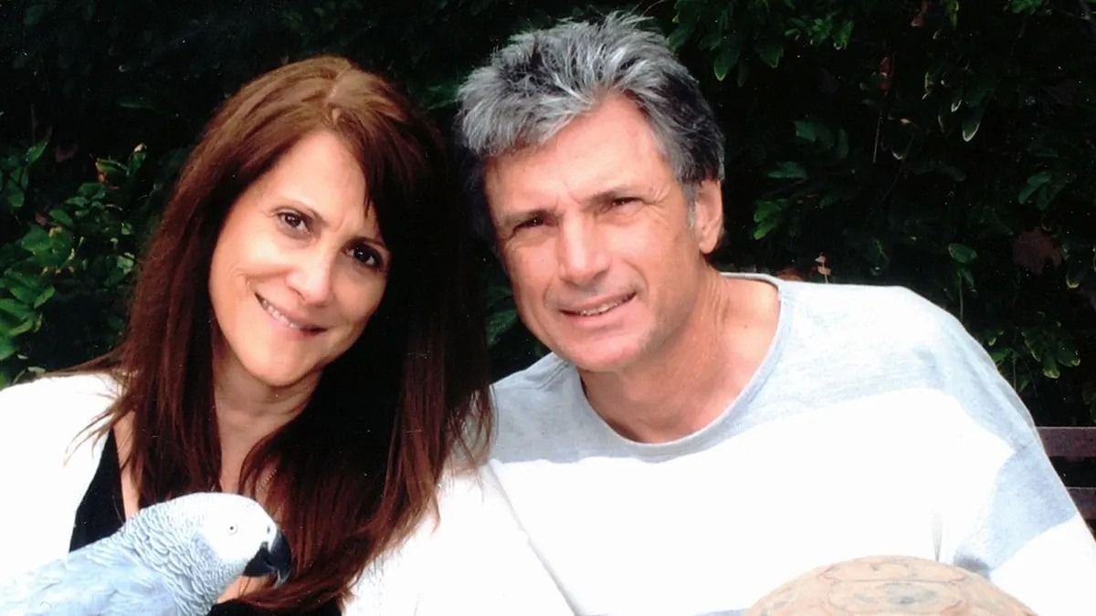 Smiling couple outdoors in casual attire against green foliage