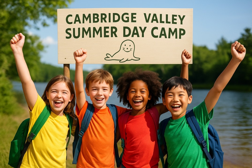 Children smiling in front of a “Cambridge Valley Summer Day Camp” sign by a lake.
