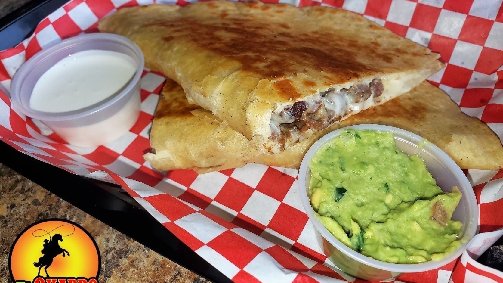 a steak quesadilla on a plate with a side of guacamole and sour cream