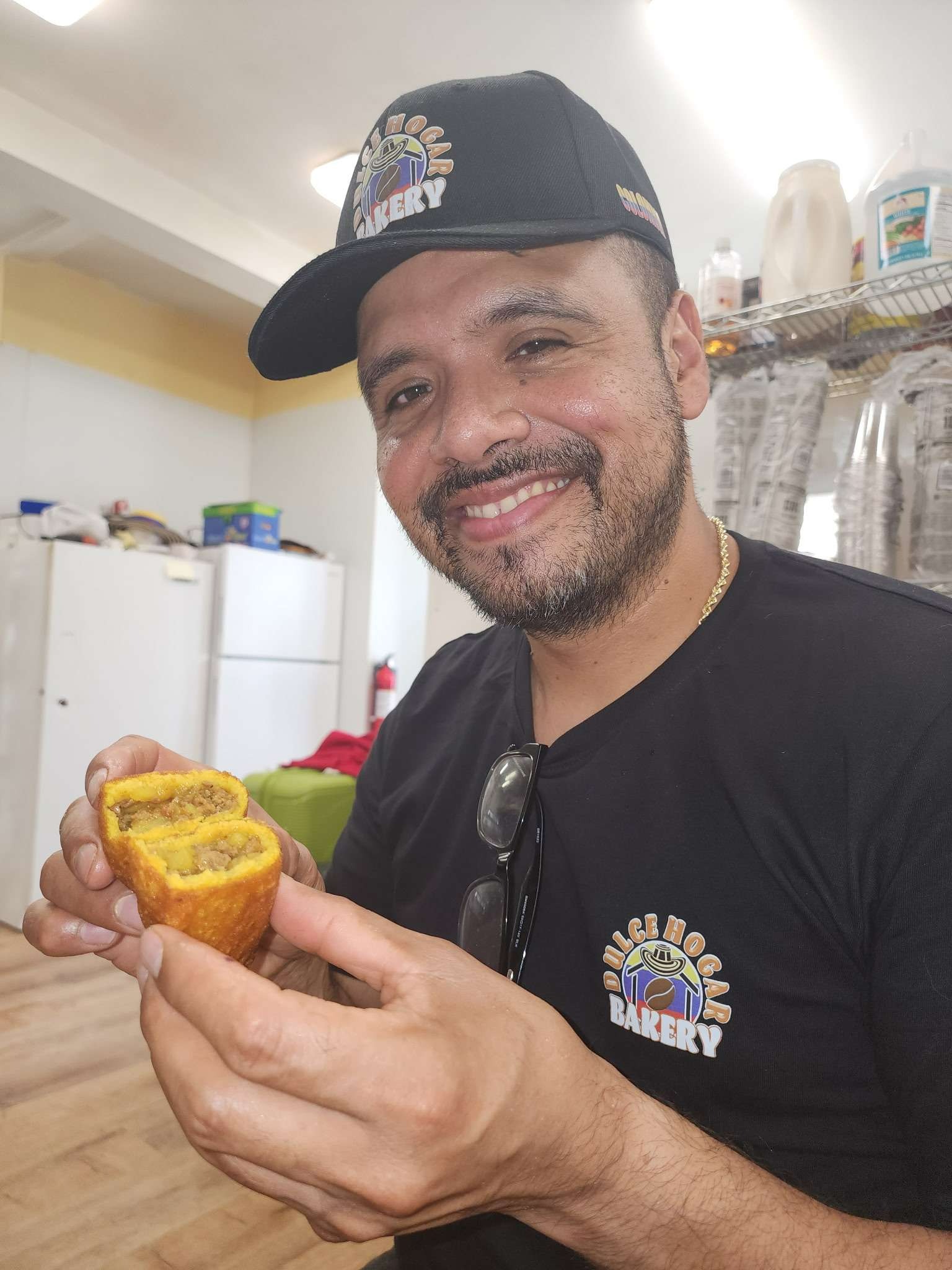 Gustavo Pineda, co-owner of Dulce Hogar Bakery, smiling while holding a freshly made empanada inside the North Tonawanda restaurant.