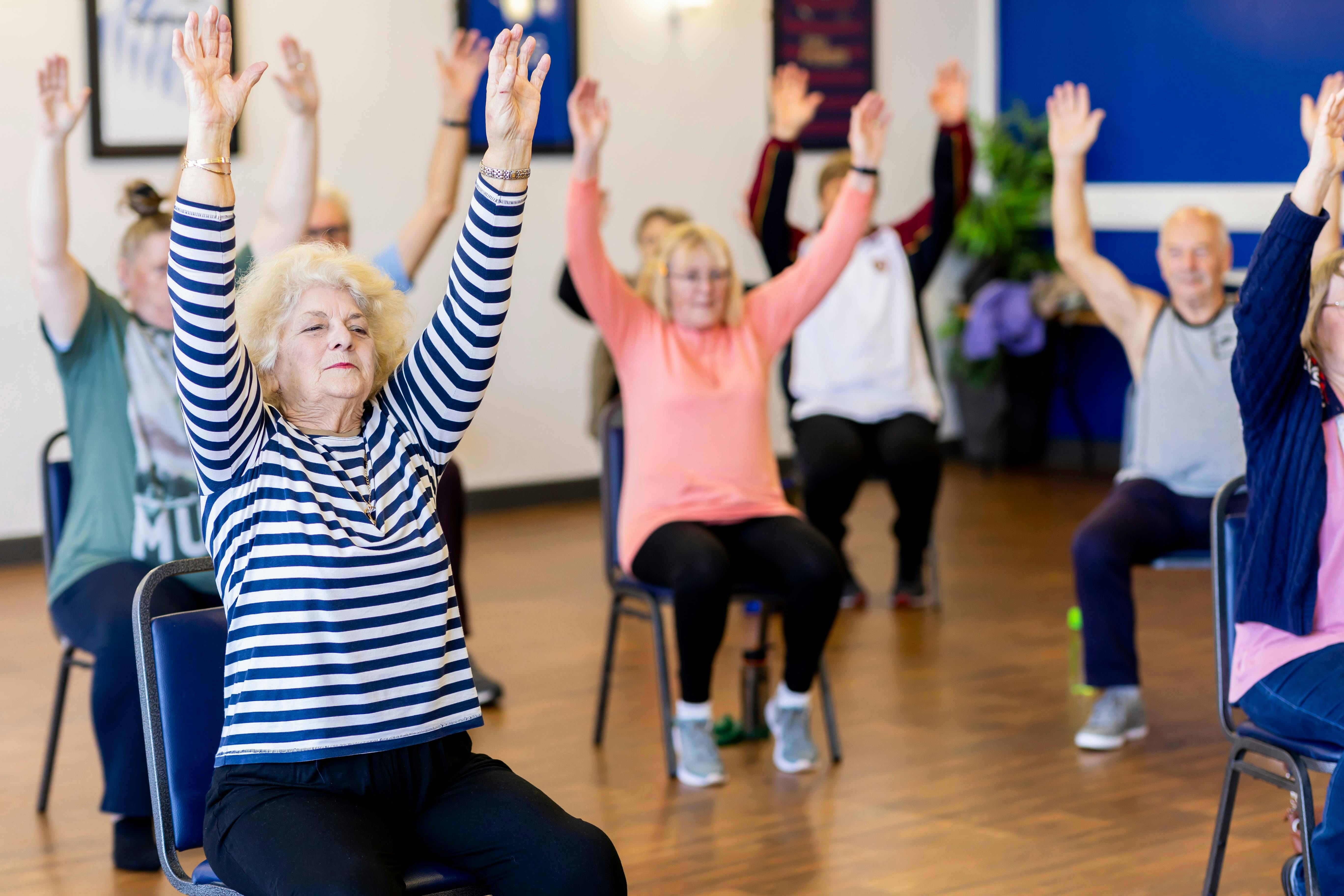 Joyful adults of various ages enjoying gentle low impact exercise in a bright fitness studio.