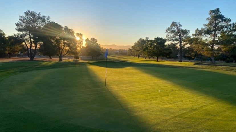 Golfer walks alone at sunrise on dew-covered Green Tree Golf Course green.