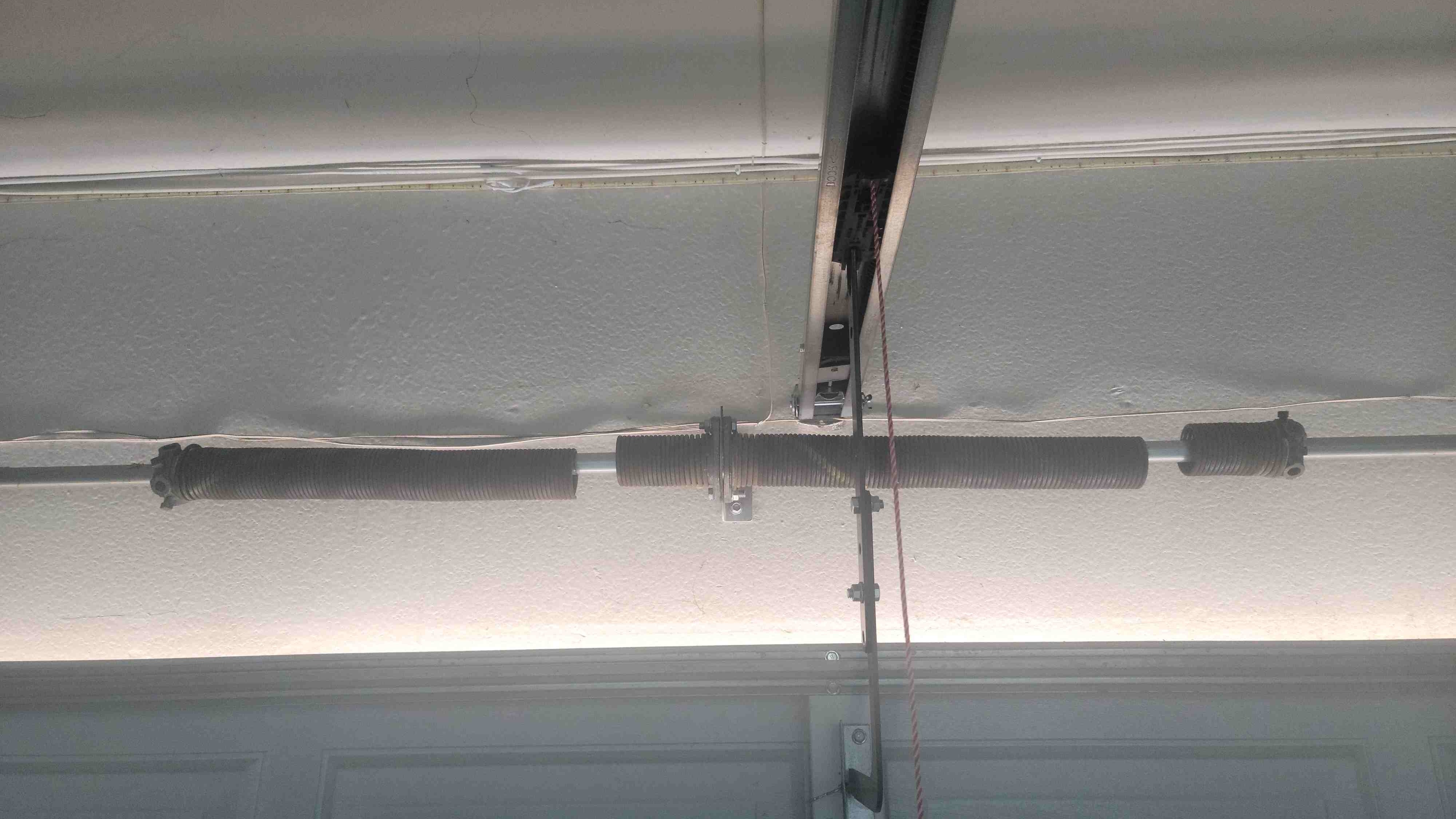 View of broken torsion springs above the garage door and garage door opener rail.