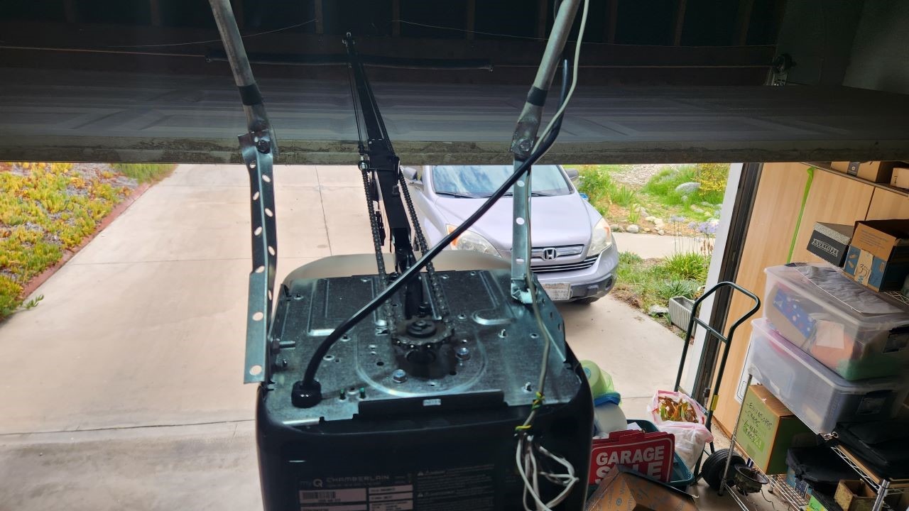 Overhead view of badly installed garage door opener with very flimsy DIY mounting hardware that is breaking.