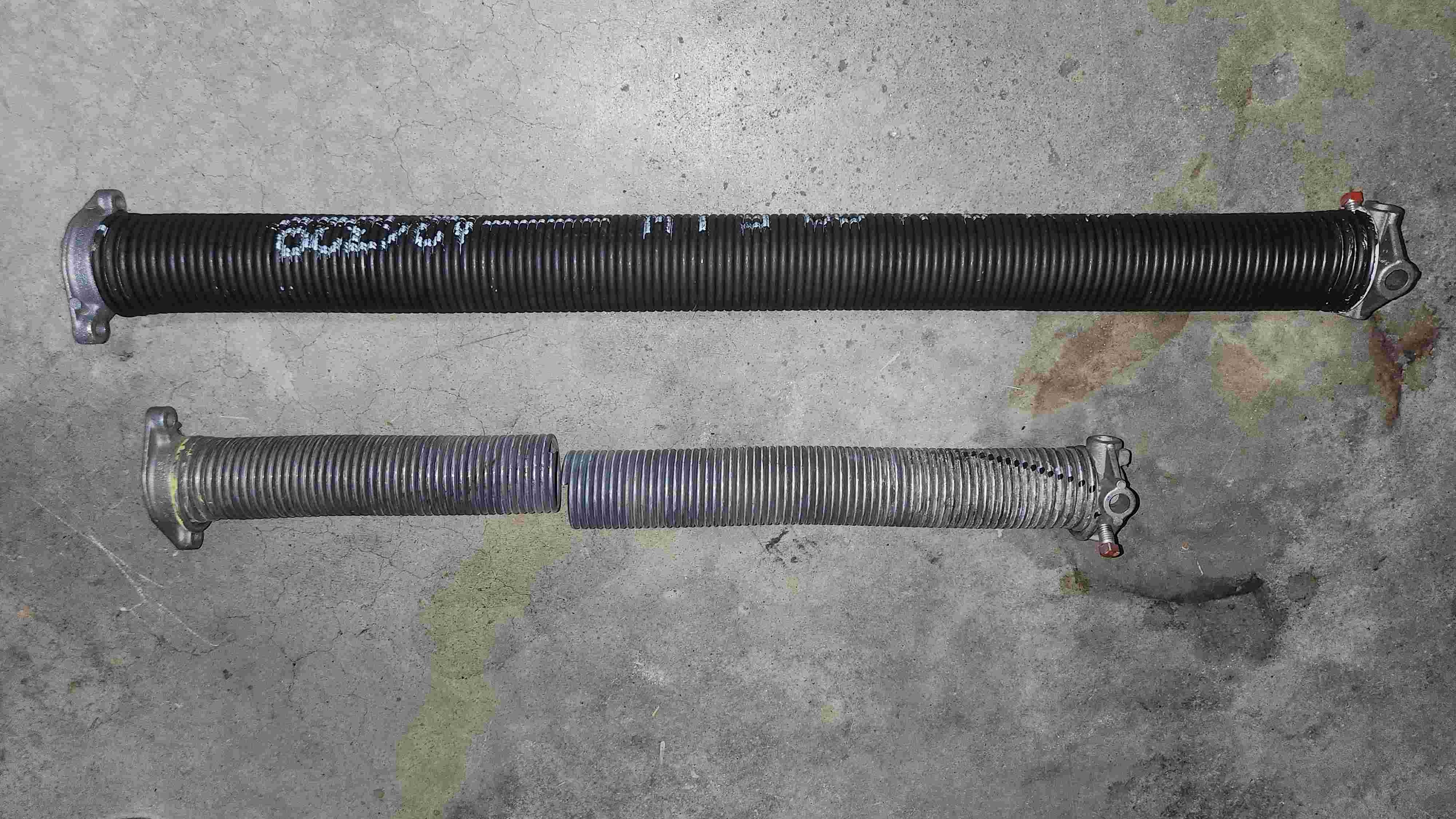 Detailed close-up of a tense metallic garage door torsion spring, showing the larger springs we use that last 4x longer than average.