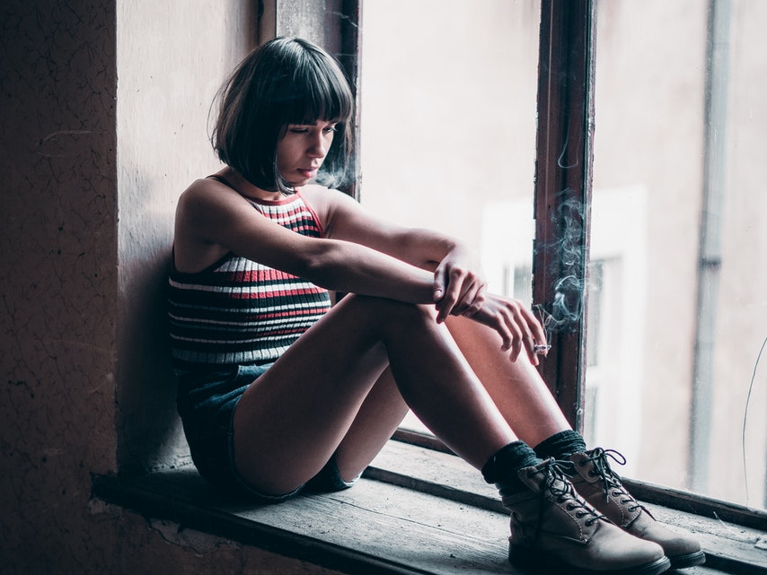 depressed girl sitting on window sill, represents an oganization that had custom data programming done