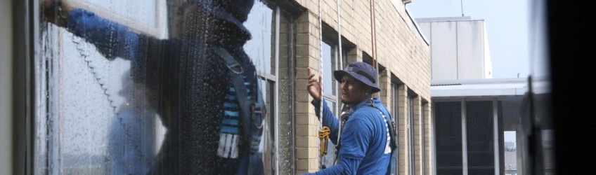 Man Hanging on building cleaning windows in construction apparel
