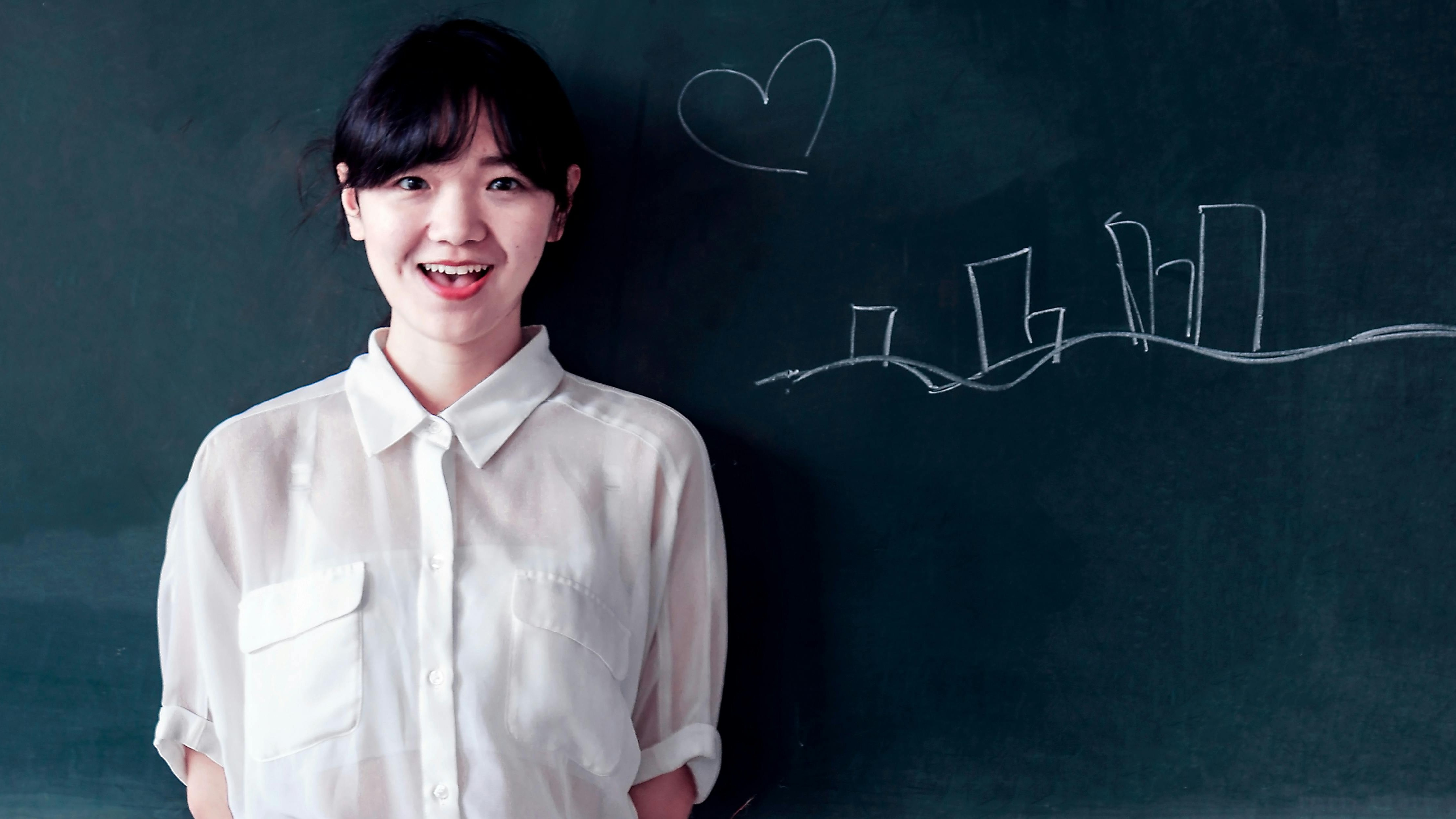 Young teacher smiling in front of a chalkboard, teaching abroad opportunities for new graduates