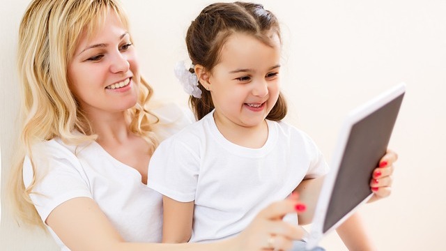 Child using a tablet on the couch, exploring the impact of tablets on childcare.