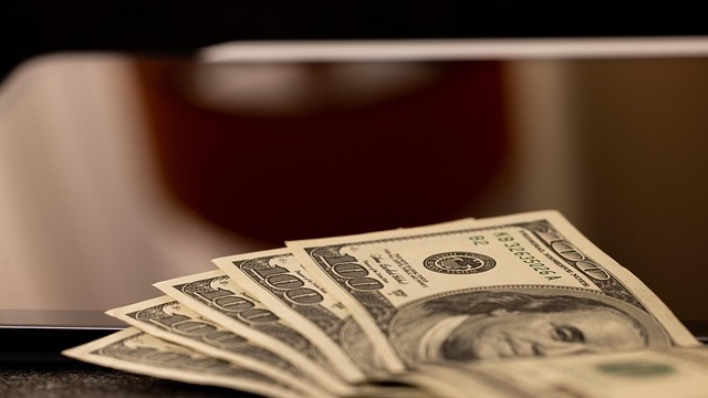 Close-up of hands holding hundred-dollar bills, flat salary increases 2026.
