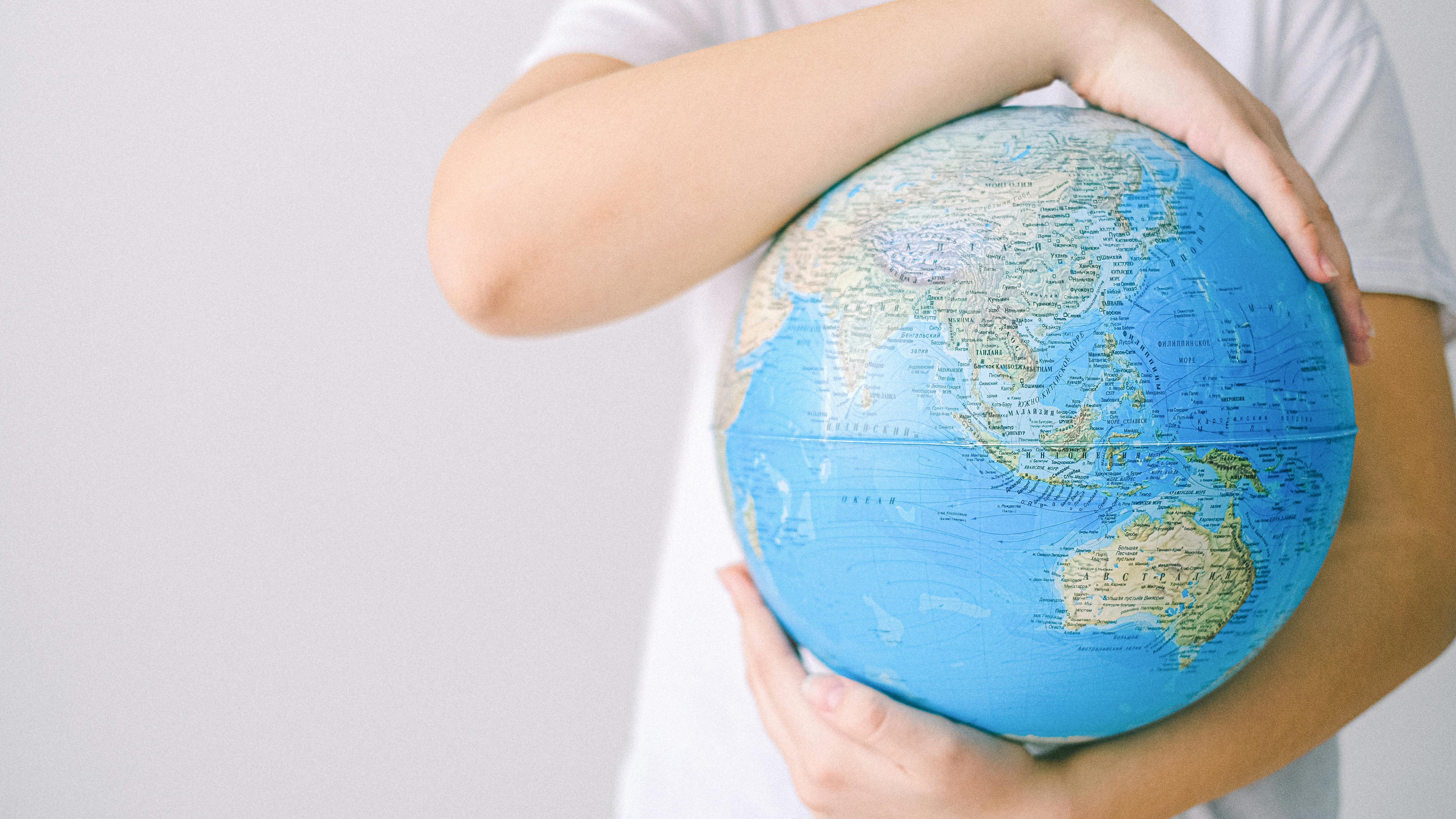 Hand holding globe in front of scenic mountain landscape; What Travel Teaches You That Nothing Else Can.