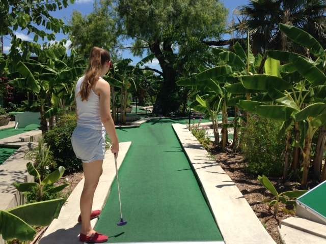 Friends competing in lively mini golf at Cool Crest, retro obstacles and sunny day