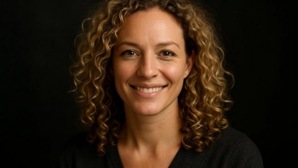 A cheerful blonde woman smiling against a dark background.