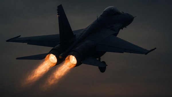 Fighter jet taking off with afterburners in a dusky sky.