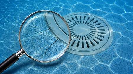 Magnifying glass highlighting cracks near a residential swimming pool main drain seal