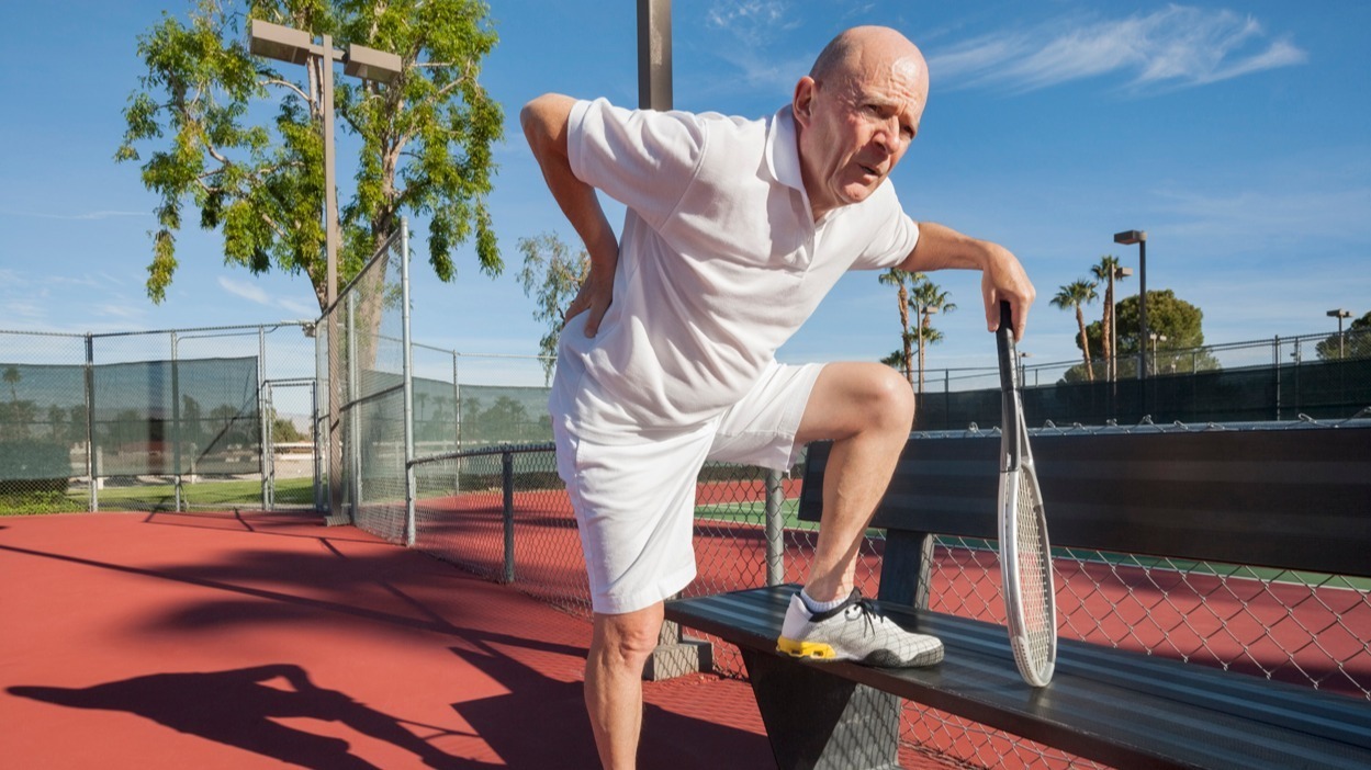 elderly man hold back in pain while playing tennis
