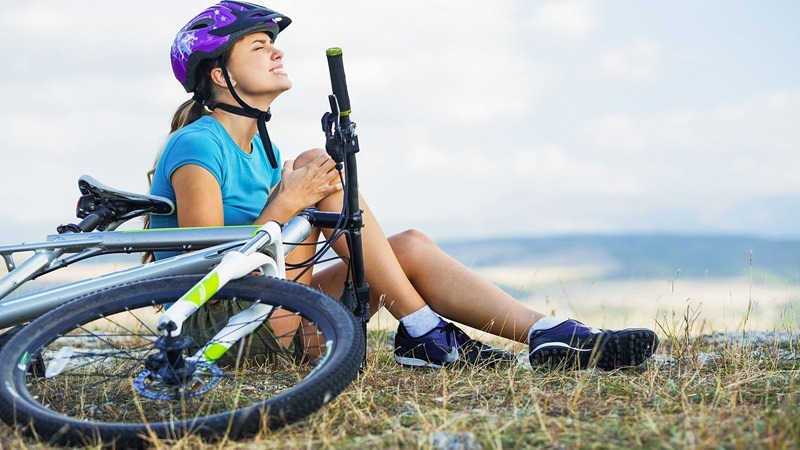female bicyclist sitting on ground holding knee her in pain