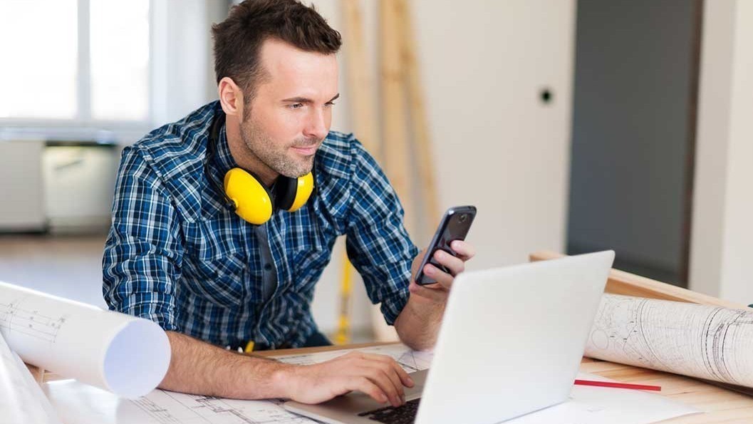 solar contractor at desk on mobile phone and computer.