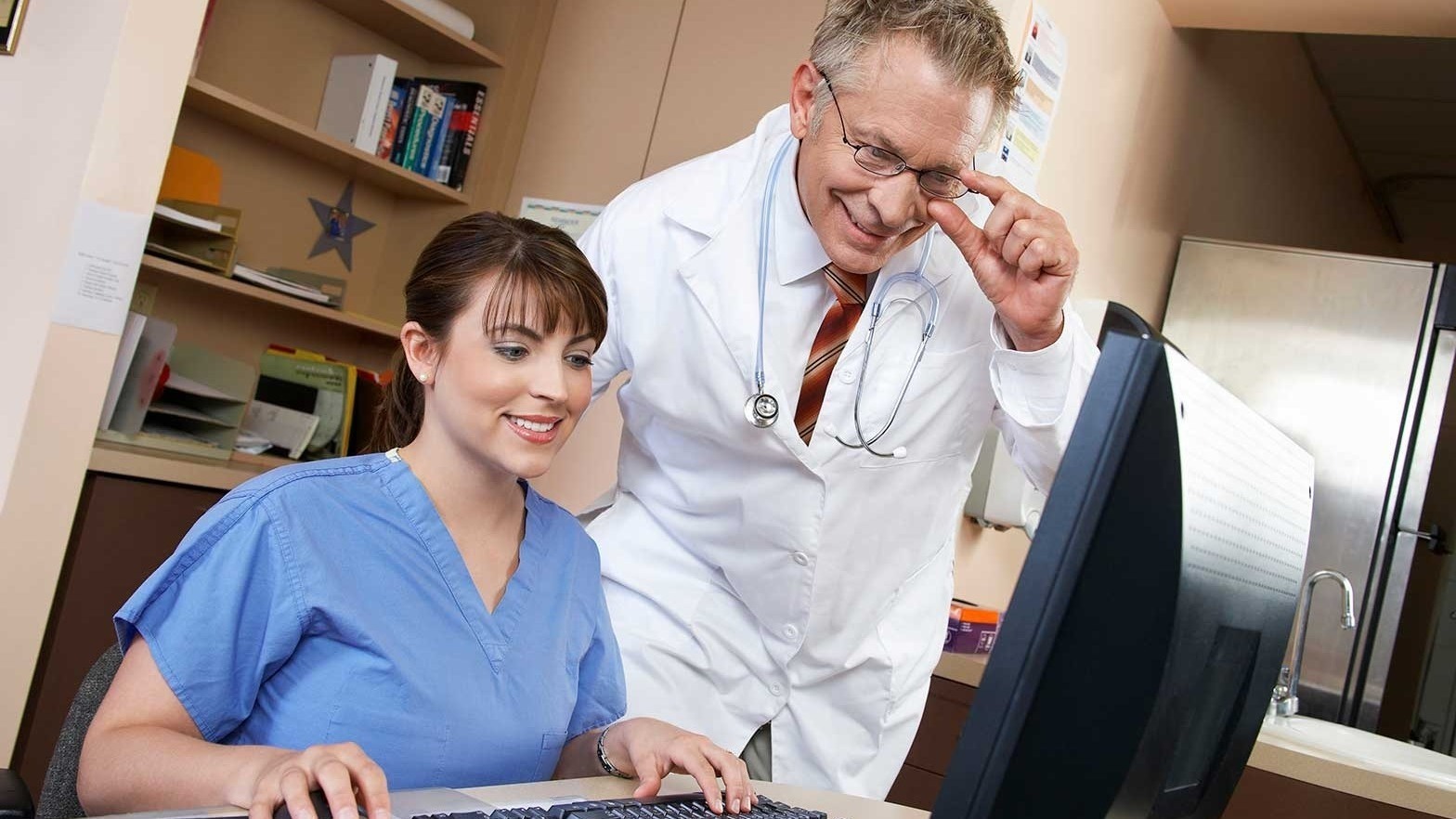 Doctor standing and nurse sitting smiling at computer.