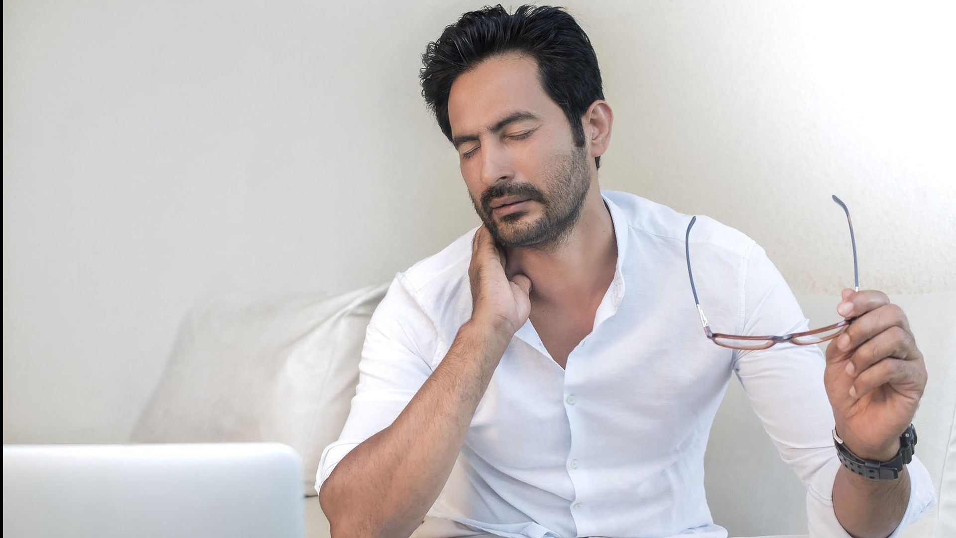 man sitting in front of computer holding his neck in pain