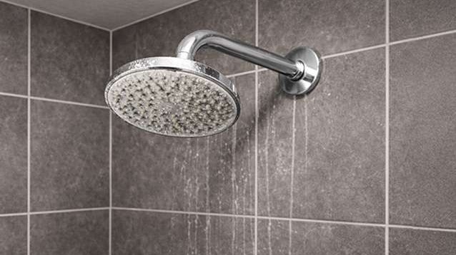 Close-up of shower head and tiles with signs of mineral buildup.
