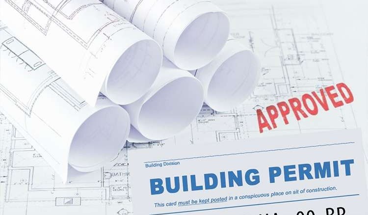Rolled architectural blueprints with a building permit document and an approved stamp on top.