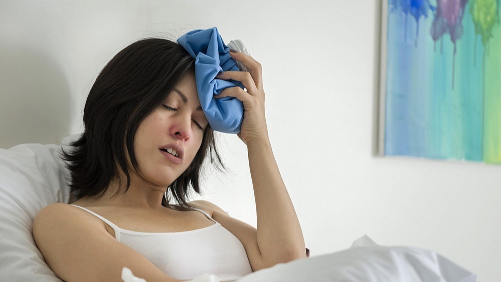 woman in bed with ice pack on head for a migraine