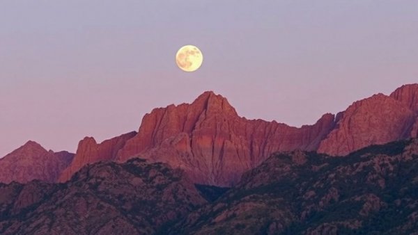 Gibbous moon glowing over rugged mountains at dusk.