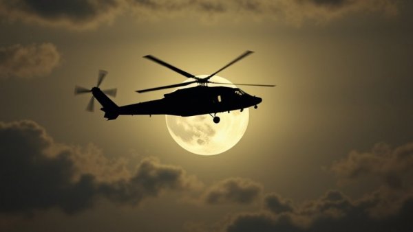 Military helicopter silhouetted against moon in twilight sky, Syria Iraq troop withdrawal.