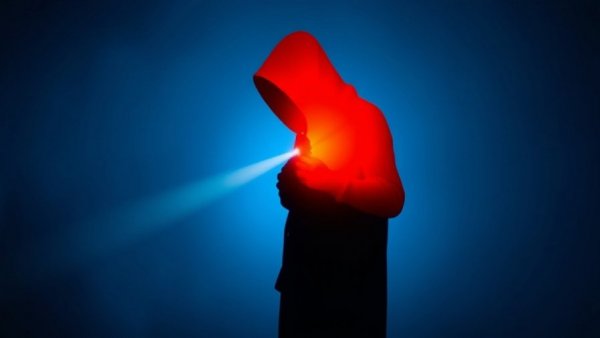 Shadowy figure with flashlight highlighting orange shape, blue background.