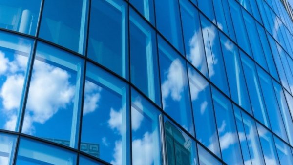Curved glass facade reflecting sky, symbolizing EU and big tech dynamics.