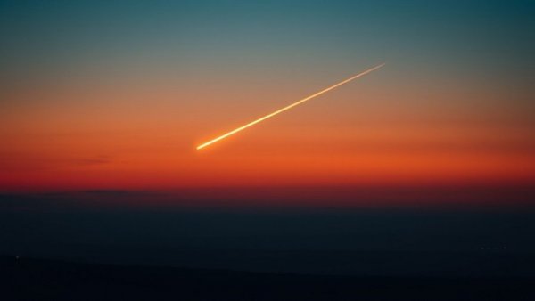 Comet with luminous tail over twilight landscape.