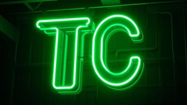 Green neon 'TC' sign glowing in a dark environment, startup funding surge Q1 2026.