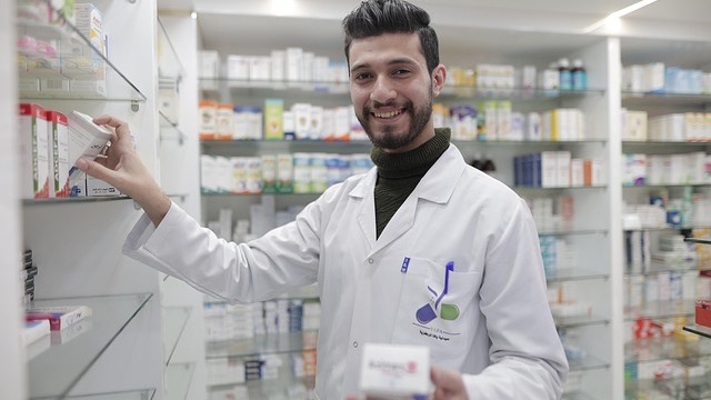 Smiling female pharmacist writing notes in a pharmacy aisle for National Pharmacist Day January 12.