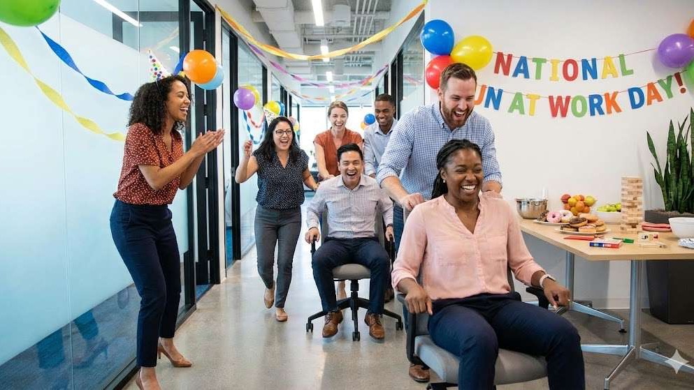 Joyful office team celebrating National Fun At Work Day with chair races.
