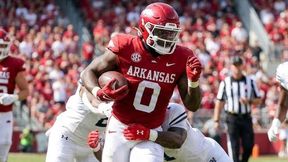 Football player sprinting across field in action, bright stadium background.