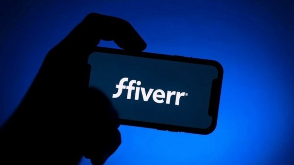 Silhouette of hand with smartphone displaying Fiverr logo.