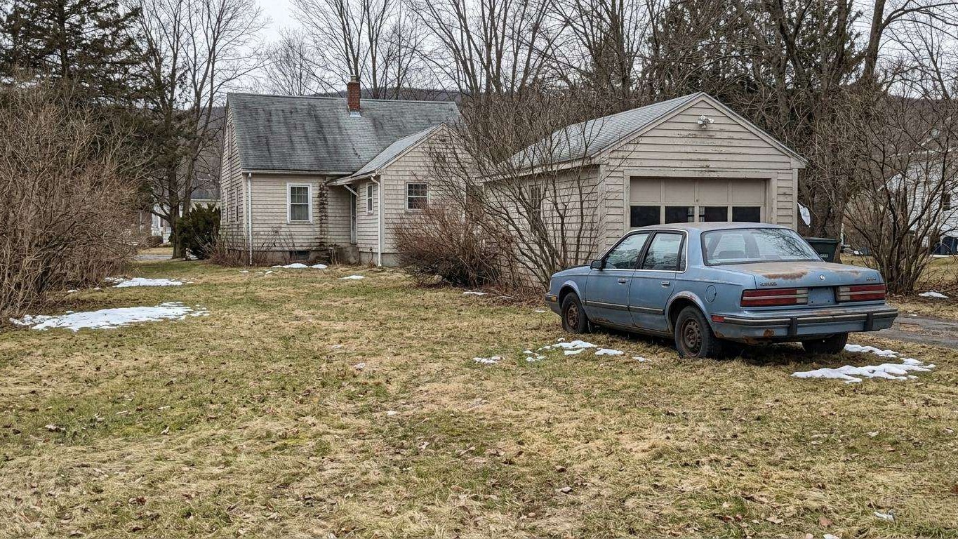 Peaceful backyard in upstate New York, featuring a modest home and older vehicle.