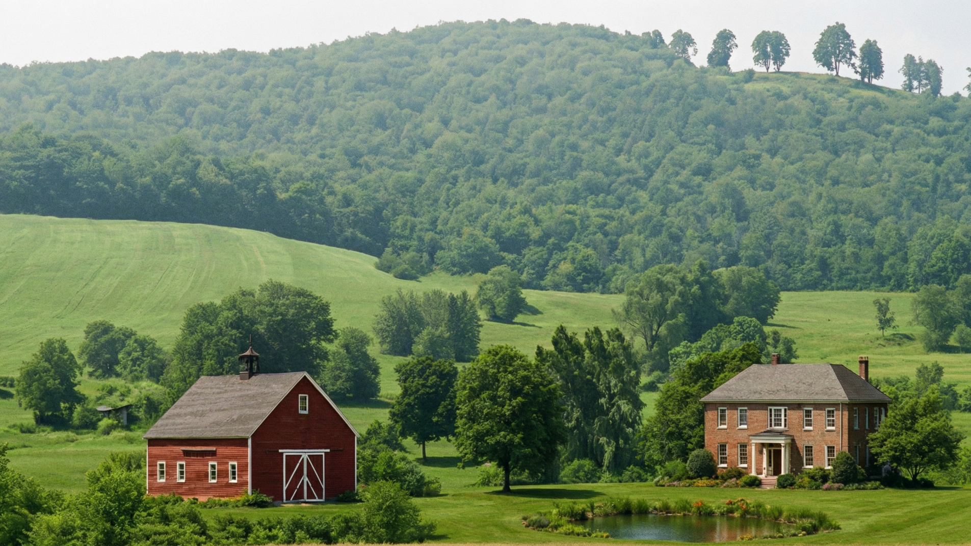 Photograph of a rural landscape with a stately brick farmhouse surrounded by manicured landscaping, a small pond in the foreground, and a traditional red barn with a cupola to the left. Rolling green hills and a dense forest form the background under a clear blue sky.