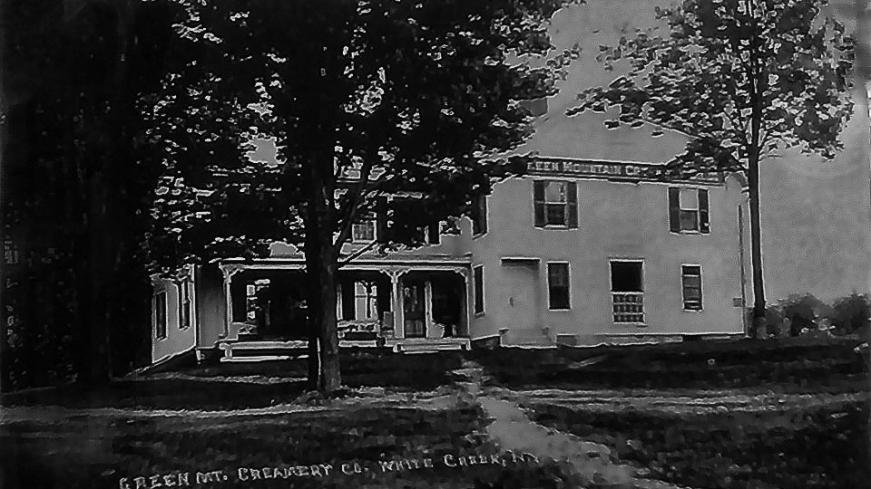 Black-and-white photograph of the Green Mountain Creamery in White Creek, NY, taken around the early 20th century. The image shows a two-story building with a porch, flanked by large trees, and a sign reading 'Green Mt. Creamery Co., White Creek, N.Y.' on the upper facade. The surrounding area includes a dirt path and grassy lawn, reflecting the rural setting of the time.