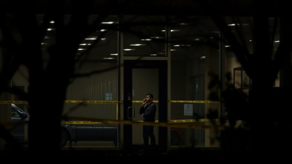 Investigation scene at a building with security tape and officer.
