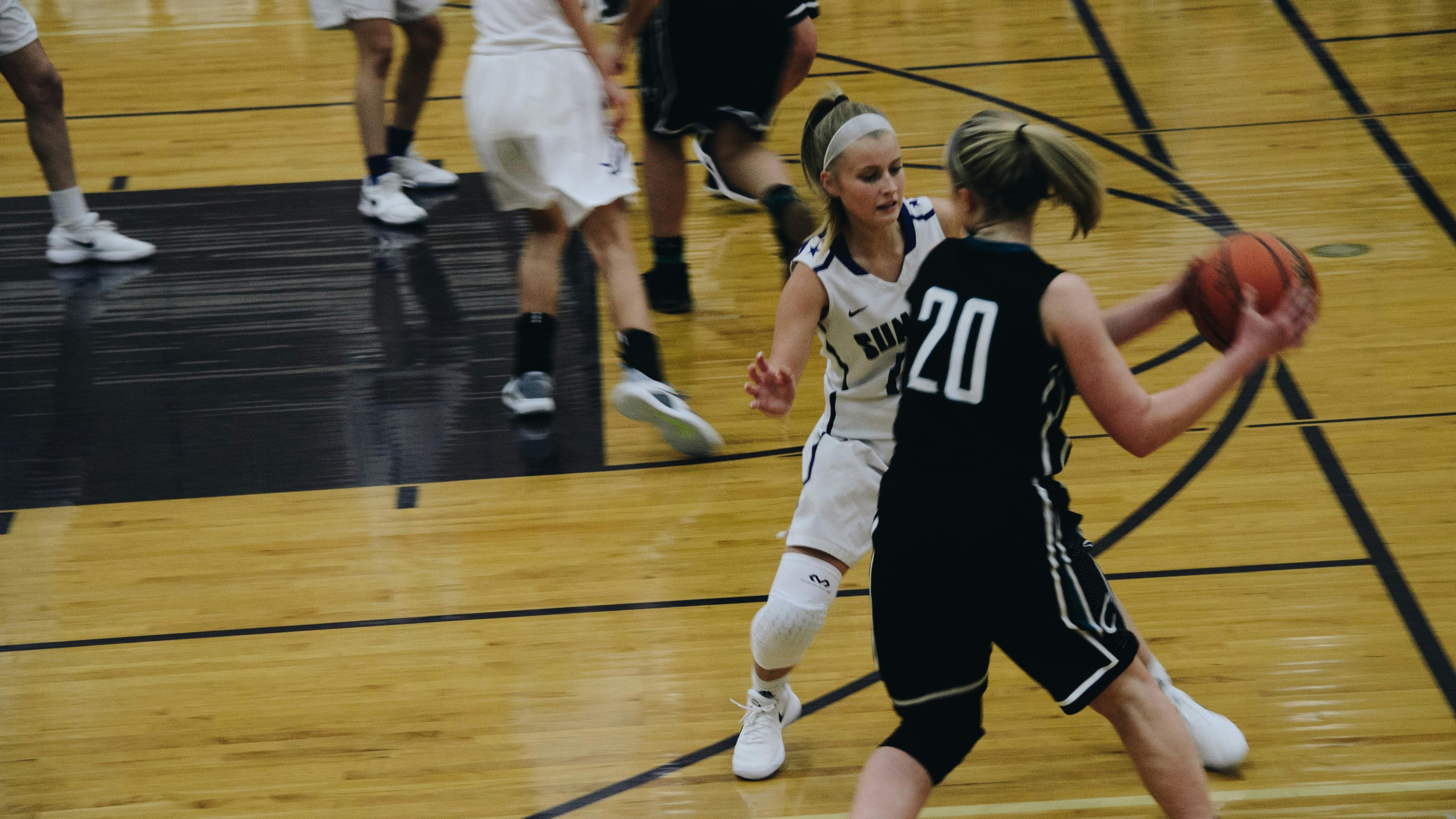 Intense play between female collegiate basketball players in a dark gym.