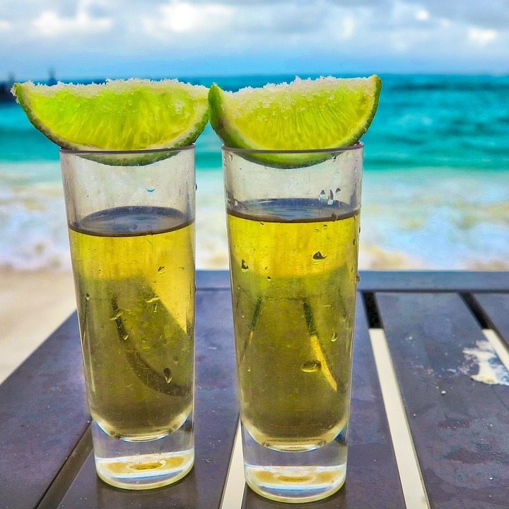 2 shots of tequila with limes on a table on the beach