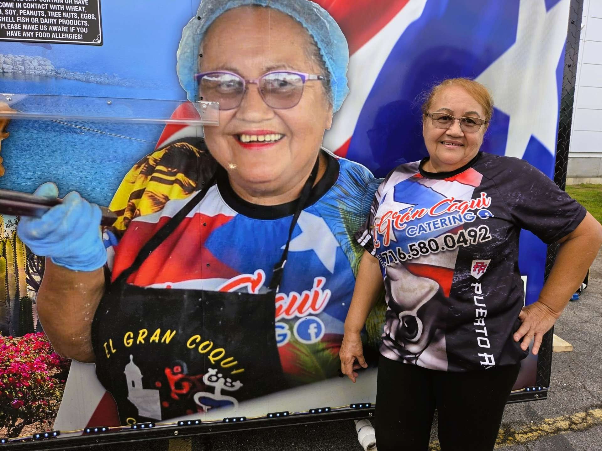 Grandmother of the El Gran Coqui Catering family standing beside her image on the Puerto Rican food trailer