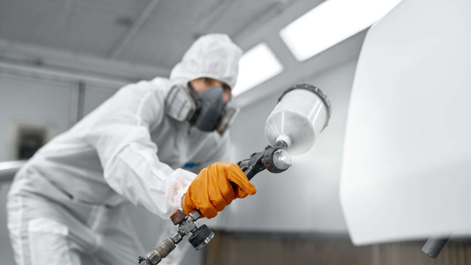 auto body paint technician applying color in paint booth for collision repair process