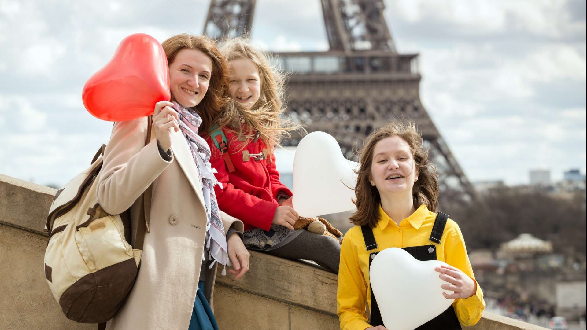 Mom and daughters with heart balloons smiling in front of the Eiffel Tower